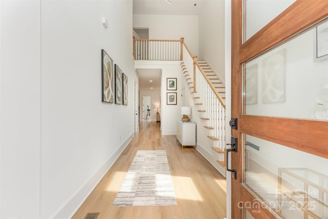 hallway featuring baseboards, light wood finished floors, stairs, and a towering ceiling