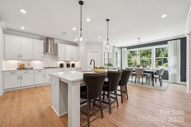 424 Balboa St, Matthews, NC 28104 - kitchen with wall chimney range hood, crown molding, an island with sink, white cabinets, and light countertops