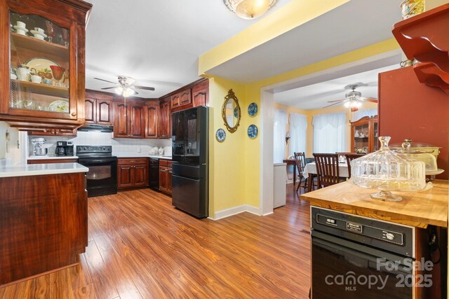 kitchen with a ceiling fan, black appliances, wood finished floors, and backsplash