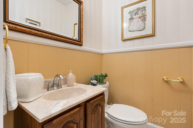 bathroom featuring vanity, toilet, a wainscoted wall, and a decorative wall