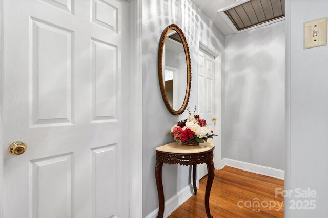 hallway with baseboards, wood finished floors, and visible vents