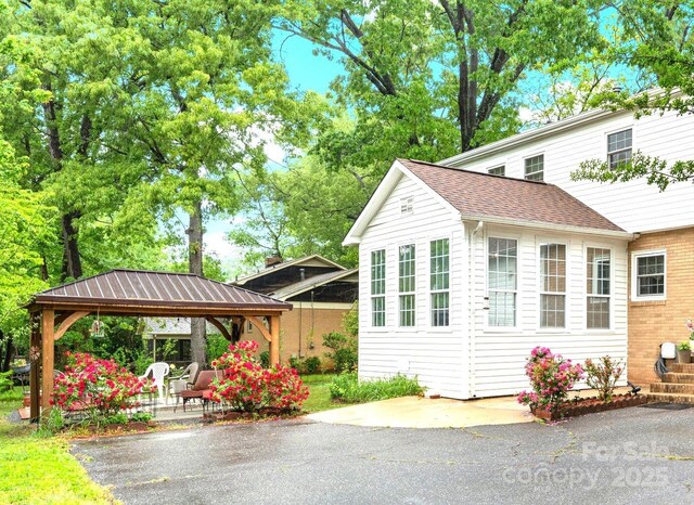 view of side of property featuring roof with shingles, a carport, a gazebo, and a patio