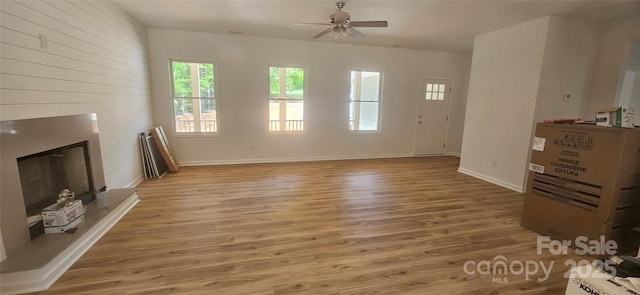unfurnished living room with a large fireplace, wood finished floors, a ceiling fan, and baseboards