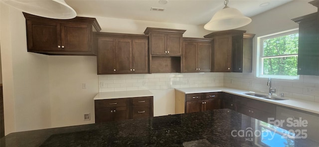 kitchen featuring visible vents, a sink, dark stone counters, decorative backsplash, and hanging light fixtures