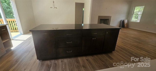 kitchen with a fireplace, wood finished floors, a kitchen island, and baseboards