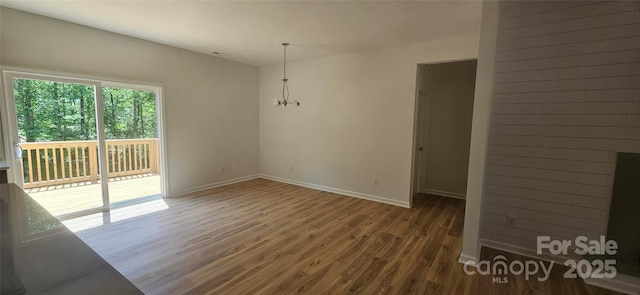 empty room featuring baseboards, wood finished floors, and an inviting chandelier