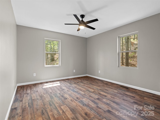 empty room with visible vents, a ceiling fan, dark wood-type flooring, and a wealth of natural light