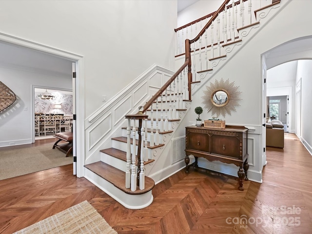 stairway with arched walkways, baseboards, a towering ceiling, and visible vents