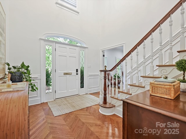 entryway with a wainscoted wall, a high ceiling, a decorative wall, and stairs