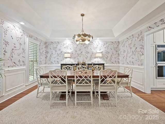 dining space with an inviting chandelier, wood finished floors, a tray ceiling, and wallpapered walls