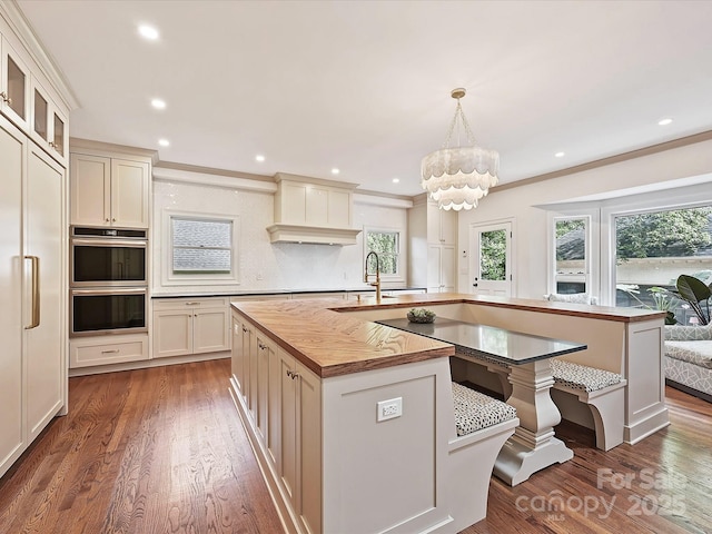 kitchen featuring double oven, a chandelier, wood finished floors, and a center island with sink