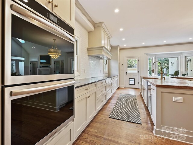 kitchen with a sink, light wood-style floors, double oven, butcher block countertops, and recessed lighting