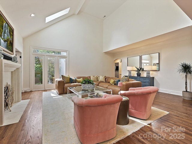 living area featuring a skylight, high vaulted ceiling, baseboards, and wood finished floors