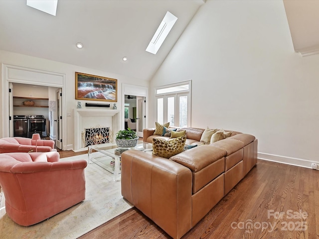 living room with a warm lit fireplace, a skylight, wood finished floors, and high vaulted ceiling