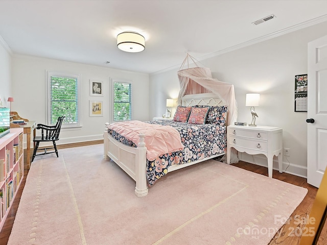 bedroom featuring baseboards, ornamental molding, wood finished floors, and visible vents