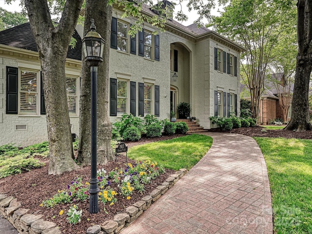 view of front of property featuring roof with shingles, a front lawn, and brick siding