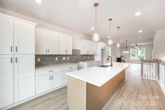 kitchen with white cabinets, a sink, an island with sink, light wood-style flooring, and tasteful backsplash