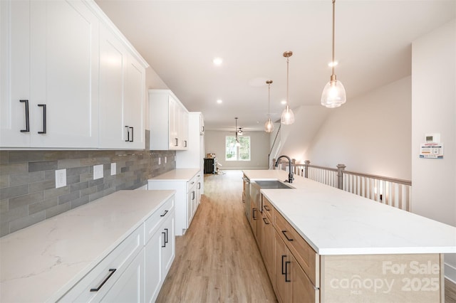 kitchen featuring backsplash, light wood-type flooring, a spacious island, a sink, and white cabinets
