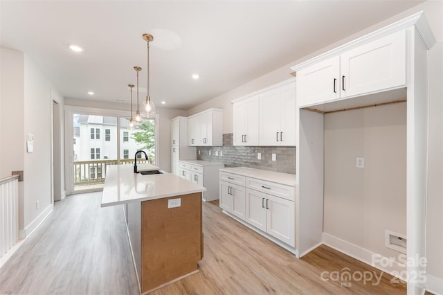 kitchen with a sink, white cabinets, light wood-style floors, and a center island with sink