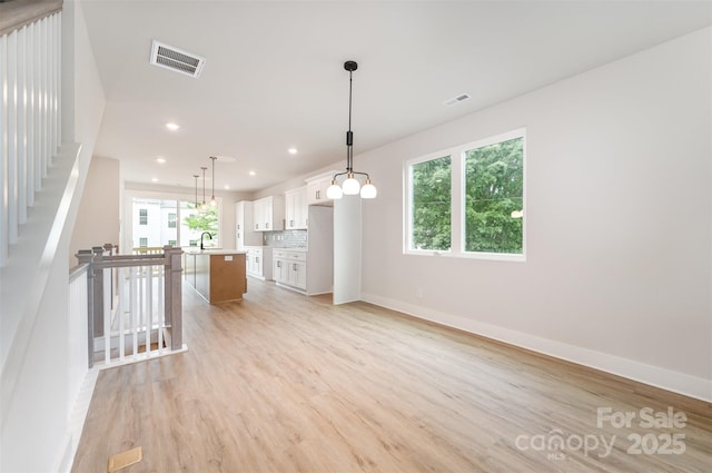 interior space with an island with sink, light wood finished floors, white cabinetry, and visible vents