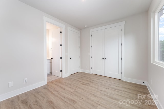 unfurnished bedroom with baseboards, ensuite bath, and wood finished floors