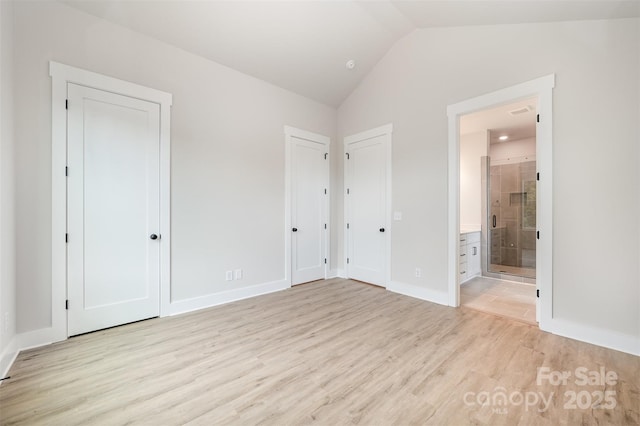 unfurnished bedroom featuring vaulted ceiling, light wood-type flooring, baseboards, two closets, and ensuite bathroom