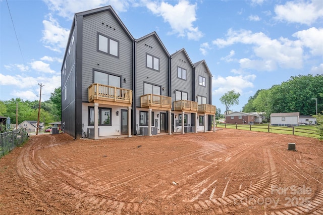 rear view of property featuring central AC unit, fence, and a balcony