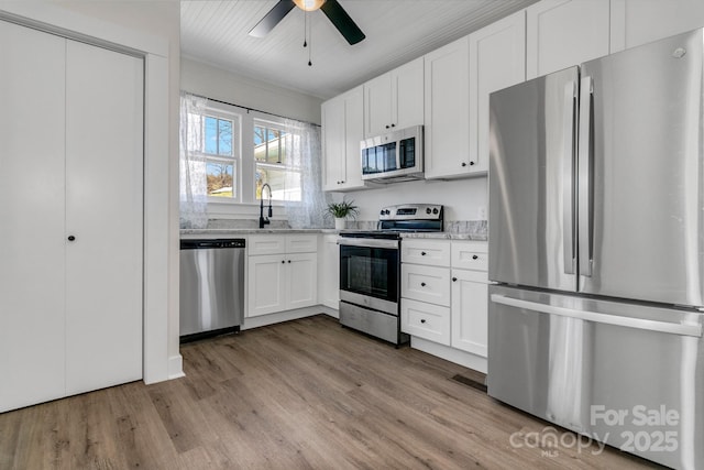 kitchen featuring appliances with stainless steel finishes, light stone countertops, wood finished floors, and white cabinetry