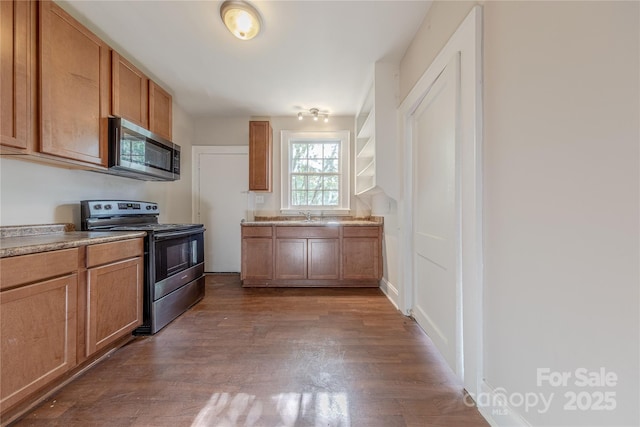 kitchen with a sink, wood finished floors, brown cabinetry, light countertops, and appliances with stainless steel finishes
