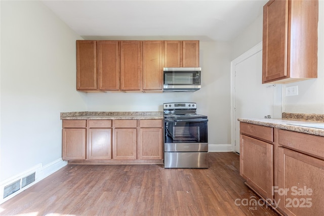 kitchen featuring baseboards, wood finished floors, visible vents, and appliances with stainless steel finishes