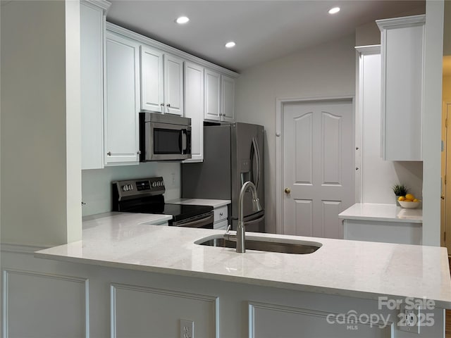 kitchen with a sink, stainless steel appliances, recessed lighting, white cabinetry, and vaulted ceiling