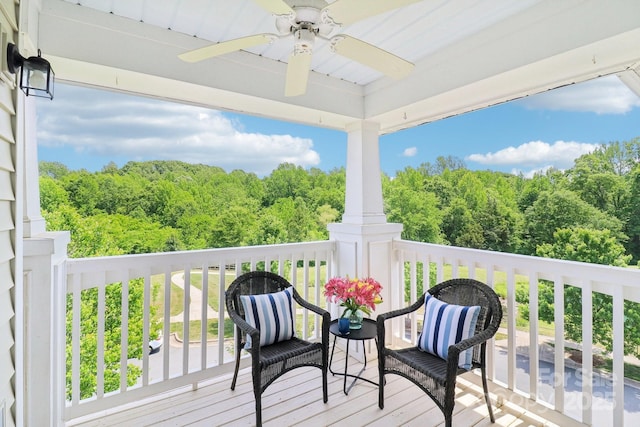 wooden terrace featuring a view of trees and ceiling fan