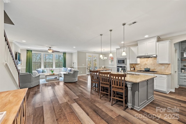 kitchen featuring dark wood-style flooring, a breakfast bar, appliances with stainless steel finishes, white cabinets, and ornamental molding