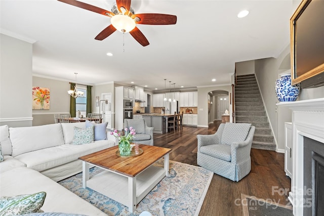 living area featuring dark wood-style floors, arched walkways, ceiling fan with notable chandelier, stairs, and ornamental molding