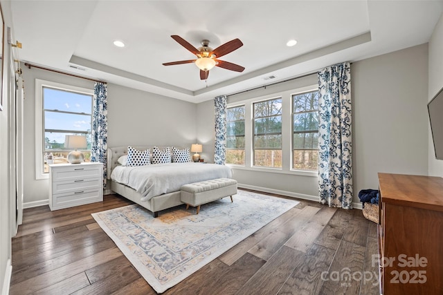 bedroom with baseboards, dark wood-style flooring, a raised ceiling, and multiple windows