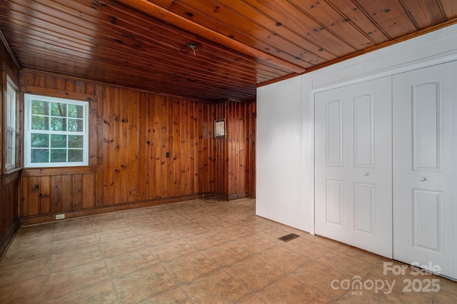 unfurnished room with wooden walls, wood ceiling, and visible vents
