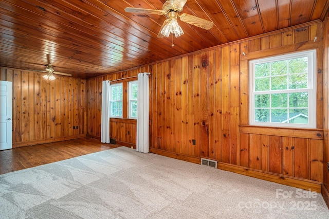 carpeted spare room with wooden walls, wooden ceiling, ceiling fan, and visible vents