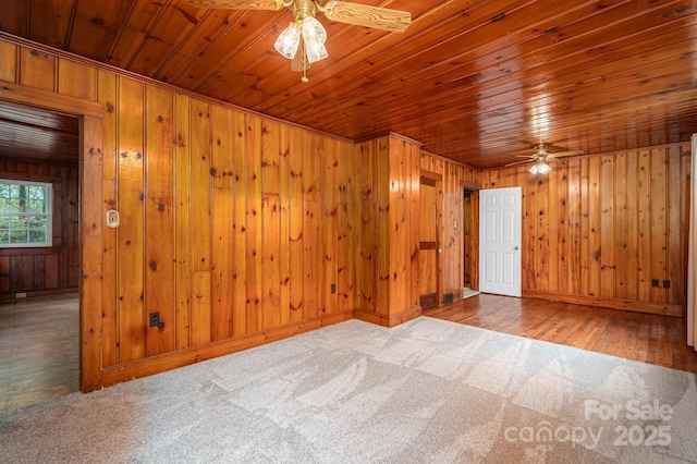 carpeted empty room featuring baseboards, wood ceiling, ceiling fan, and wooden walls