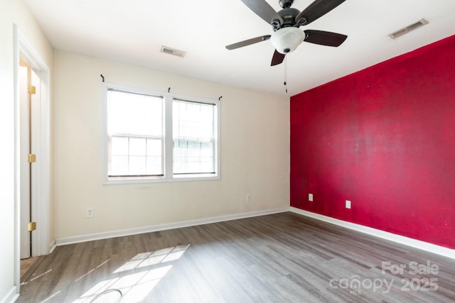 spare room featuring wood finished floors, visible vents, baseboards, and ceiling fan