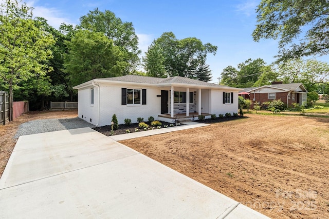 ranch-style home with covered porch, fence, driveway, and brick siding