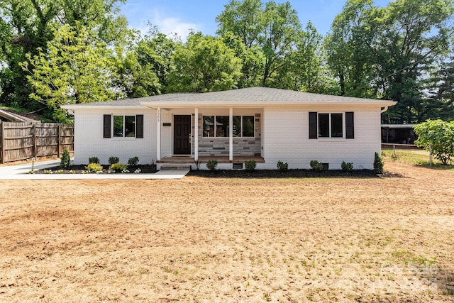 single story home with covered porch, brick siding, and fence