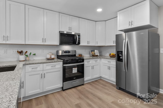 kitchen with white cabinetry, light stone countertops, appliances with stainless steel finishes, and light wood-style floors