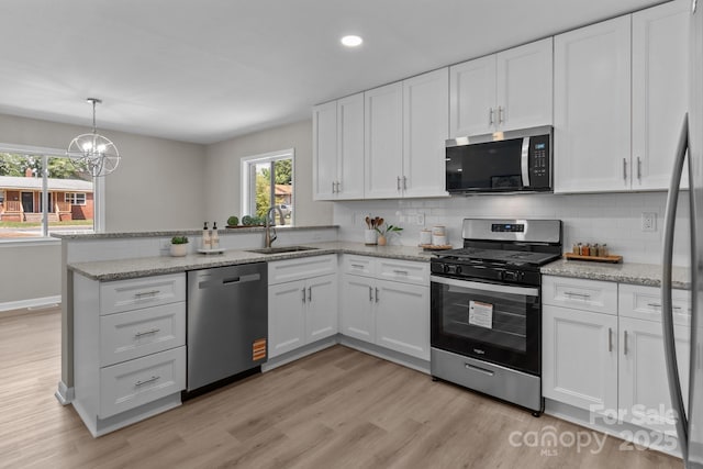 kitchen featuring appliances with stainless steel finishes, a sink, white cabinets, a peninsula, and a chandelier