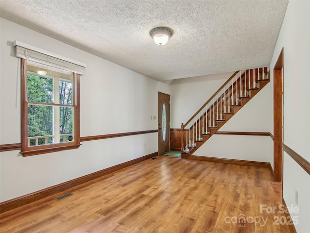 spare room featuring wood finished floors, visible vents, baseboards, a textured ceiling, and stairs