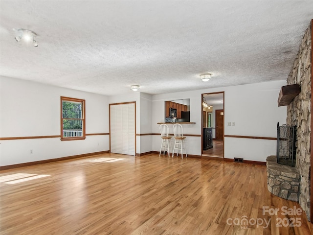 unfurnished living room with a fireplace, light wood-style flooring, a textured ceiling, and baseboards