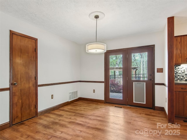 unfurnished dining area featuring a textured ceiling, wood finished floors, visible vents, and baseboards