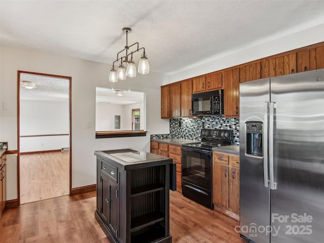 kitchen with backsplash, dark countertops, wood finished floors, and black appliances