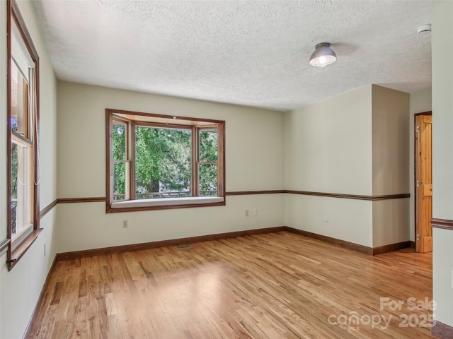 unfurnished room featuring light wood-style floors, a textured ceiling, baseboards, and visible vents