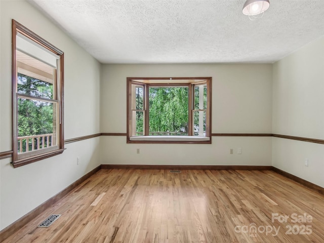 unfurnished room featuring baseboards, light wood finished floors, a textured ceiling, and visible vents