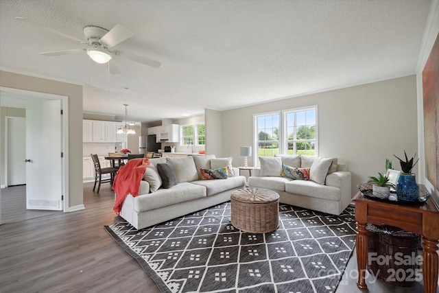 living room featuring a textured ceiling, wood finished floors, baseboards, and ceiling fan with notable chandelier